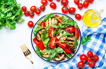 Grilled vegetables salad with paprika, zucchini, eggplant, tomatoes and spinach on plate, white table background, top view