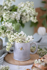 A gray cup with the image of a bee, white lilac flowers and a cake. Tea party with flowers