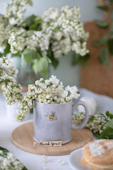 A gray cup with the image of a bee, white lilac flowers and a cake. Tea party with flowers