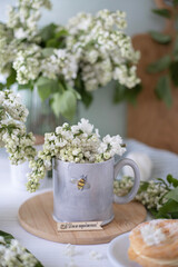 A gray cup with the image of a bee, white lilac flowers and a cake. Tea party with flowers
