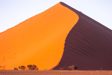 Fototapeta na wymiar Red sand dunes with car in morning sunlight in Sossusvlei, Namibia