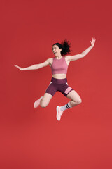 Fototapeta na wymiar Excited determined strong sportswoman, smiling and stretching her body while jumping, red background