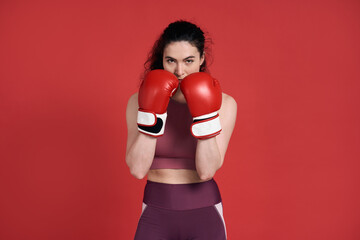 Young sporty strong fitness woman boxer fighter posing isolated over red background in boxing gloves - obrazy, fototapety, plakaty