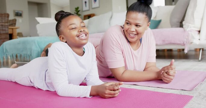 Happy unaltered african american mother and daughter lying on yoga mats talking, in slow motion