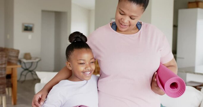 Happy unaltered african american mother and daughter holding yoga mats and smiling, slow motion