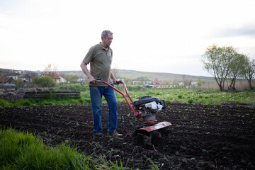 man cultivates the ground in the garden with a tiller preparing the soil for sowing