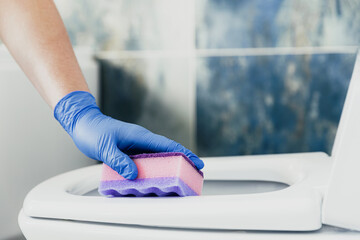 Close up on woman hand gloved in blue rubber protective gloves. Housewife cleaning toilet bowl, seat with detergent liquid, wet wipe in bathroom, restroom. Female washing, disinfecting toilet seat