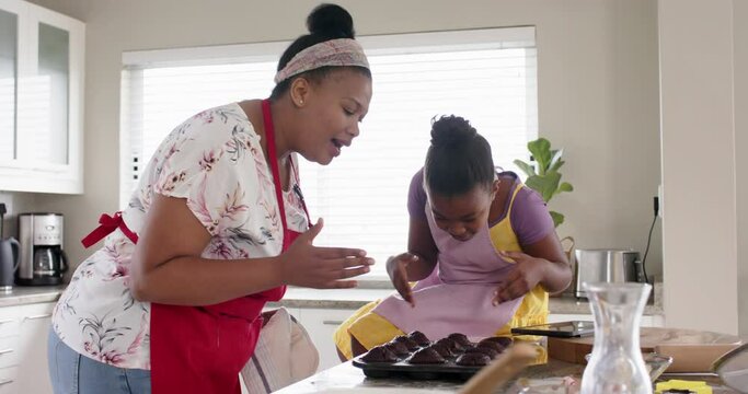 Happy unaltered african american mother and daughter baking, with cakes out of oven, in slow motion