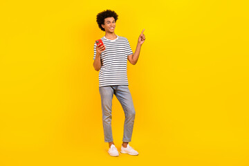 Fototapeta na wymiar Full body photo of young blogger man wear stylish look direct finger mockup phone check black friday offer isolated on yellow background