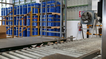 Drums holding 200 liters of chemicals are filled on a line. Inside the warehouse, stacks of blue...