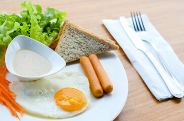 Breakfast consisting of fried eggs, smoked sausages Bread and Caesar Salad
