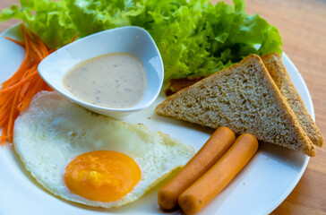 Breakfast consisting of fried eggs, smoked sausages Bread and Caesar Salad