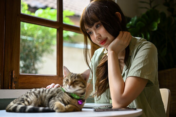 Charming young Asian woman resting and petting with her cute adorable tabby cat