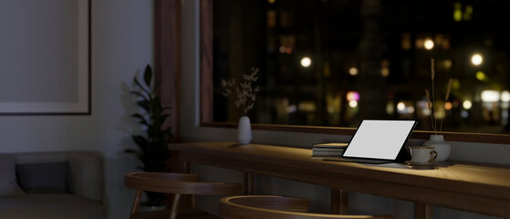Workspace with tablet mockup on a wooden table against window in a dark cozy living room.