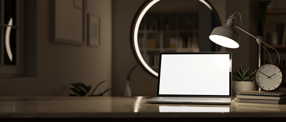 Home workspace at night with laptop mockup, table lamp, alarm clock and decor