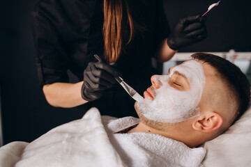 Obraz na płótnie Canvas Man getting facial nourishing mask by beautician at spa salon, closeup. Apply face mask