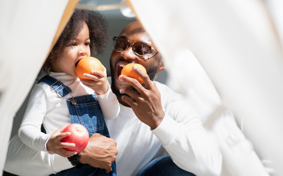 Happy Multiracial Family Having Fun At Home Together. Portrait Of Multiethnic Father And Little Biracial Daughter Playing With Apple At Backyard Camping. Diverse Ethnic Dad Laughing With Cheerful Kid.