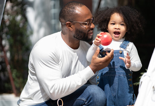 Happy Multiracial Family Having Fun At Home Together. Portrait Of Multiethnic Father And Little Biracial Daughter Playing With Apple At Backyard Camping. Diverse Ethnic Dad Laughing With Cheerful Kid.