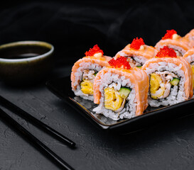 Sushi roll with fried salmon on black plate