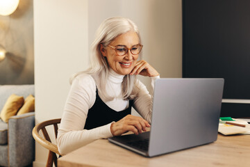 Happy senior woman working with a laptop in her home office