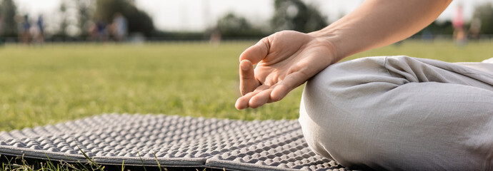 cropped view of yoga man meditating and showing gyan mudra gesture on yoga mat and green grass...