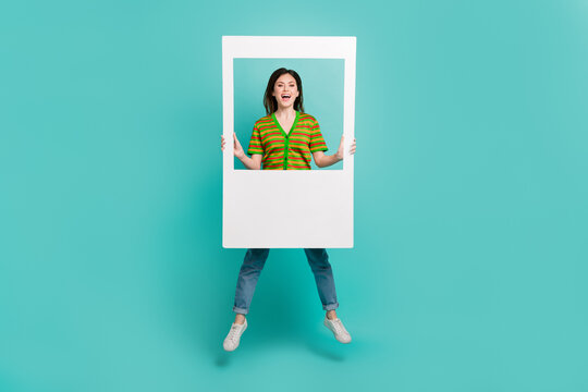 Full length photo of sweet excited woman dressed striped cardigan jumping high holding frame isolated teal color background