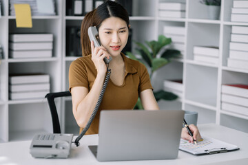 Asian businesswoman involved in cellphone call conversation working on computer, giving professional consultation to client or negotiating project.