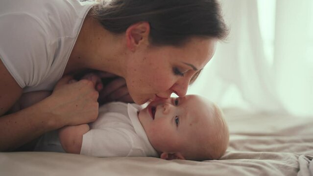 Happy mom babysitting little baby smiling talking at home in maternity leave. Motherhood babycare concept. Mother looking at her positive laughing kid. Babyhood, childhood, parenting, maternity leave.