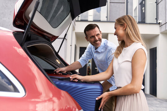 Caucasian couple packing luggage into car trunk for holiday