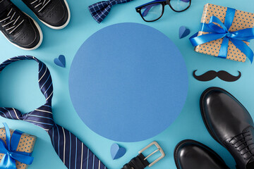 Happy Father's Day concept. Top view flat lay of gift boxes, black shoes, baby sneakers, paper mustache, male accessories and hearts on light blue background with blank circle for text or advert