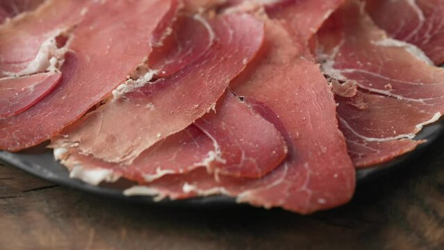 plate of sliced spanish iberico ham on wooden table background, rotating