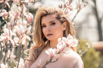 Fototapeta premium Portrait of a beautiful happy middle aged woman enjoying the smell in a blooming spring garden. Beautiful magnolia bushes, large flowers.