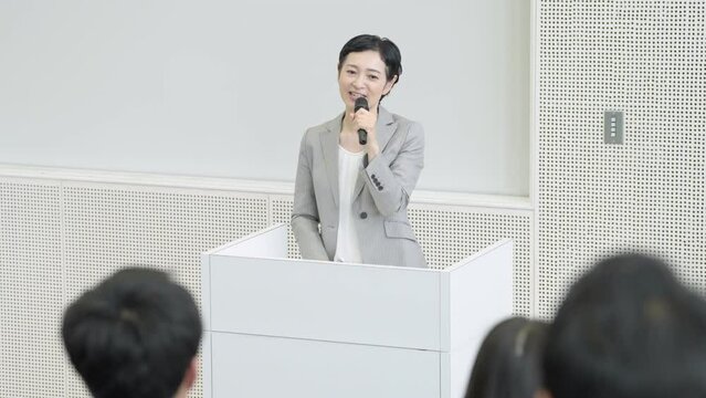 セミナーでマイクを持って話す女性（講師・教員）