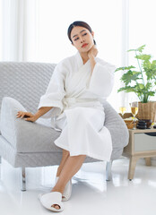 Millennial Asian young beautiful sexy female model in white clean bathrobe having painful backache neckache sitting holding hand massaging back and neck from office syndrome waiting for masseuse