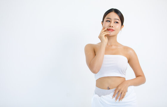 Isolated cutout studio shot millennial Asian beautiful pretty sexy female model in tube cropped top shirt standing smiling holding hand on face showing presenting painting nails on white background