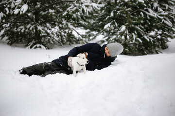 Naklejka na ściany i meble a girl with a jack Russell terrier dog playing in the snow in a clearing of a winter forest