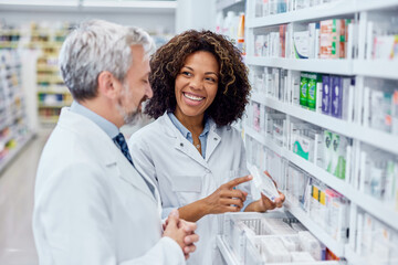 Smiling African female holding a box of medicine, talking with a male pharmacist.
