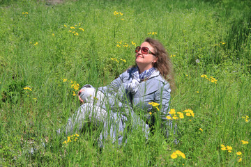 Young attractive woman enjoys the warm rays of the spring sun while sitting on the lawn.