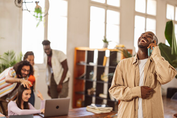 office man with coworkers in background, talking on smartphone, discussing company report with colleague on smartphone