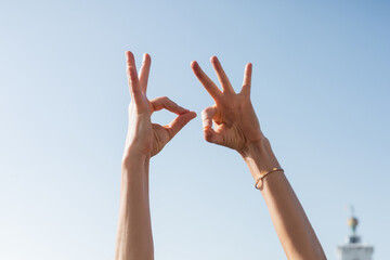 Cropped view of woman showing okay gesture with sky at background