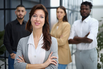 Portrait of a young woman standing in an office with colleagues in the background.