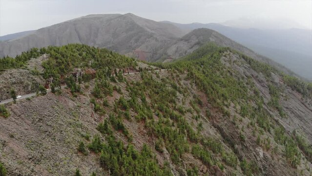 Aerial view of beautiful volcanic landscape with highway and cars driving along pine forest. 4K panoramic drone video. Volcano Teide, Tenerife, Canarias, Spain. Footage during dust storm calima 