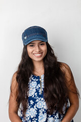 Studio shot of a young, beautiful Indian female model in casual wear wearing blue and white printed top, blue jeans and blue cap against white background. Female model. Fashion Portrait.