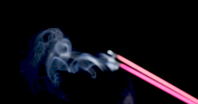 Cinematic video of burning incense sticks with smoke over a black blurred background.advertisement concept.smoldering incense sticks sandalwood stick with incense smokes on a black background close-up