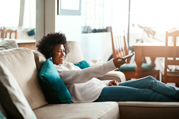 Black woman, watching tv and relax on couch with remote, home and happiness for me time, comedy or show. African girl, television and happy for movie, video or search on living room sofa in apartment