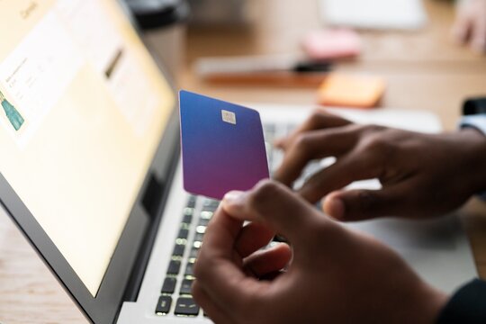 Unrecognizable male using modern laptop while entering credit card credentials into computer during online shopping