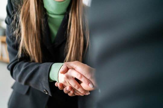 Anonymous woman and man in formal wear shaking hands while greeting each other during meeting in modern office