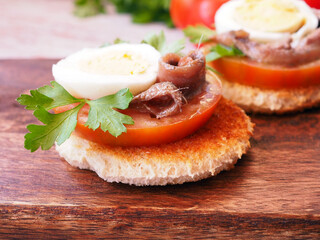Spanish appetizer: tapas with tomato, egg and anchovy on a wooden serving board