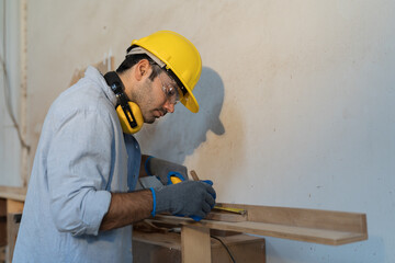 Male carpenter measure the size of wood during working in wood workshop. Male joiner wearing safety...