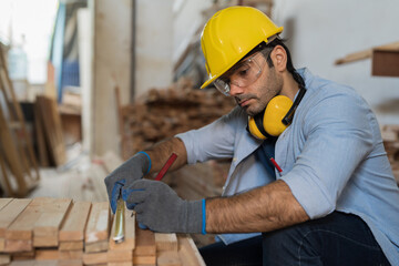 Male carpenter measure the size of wood during working in wood workshop. Male joiner wearing safety...